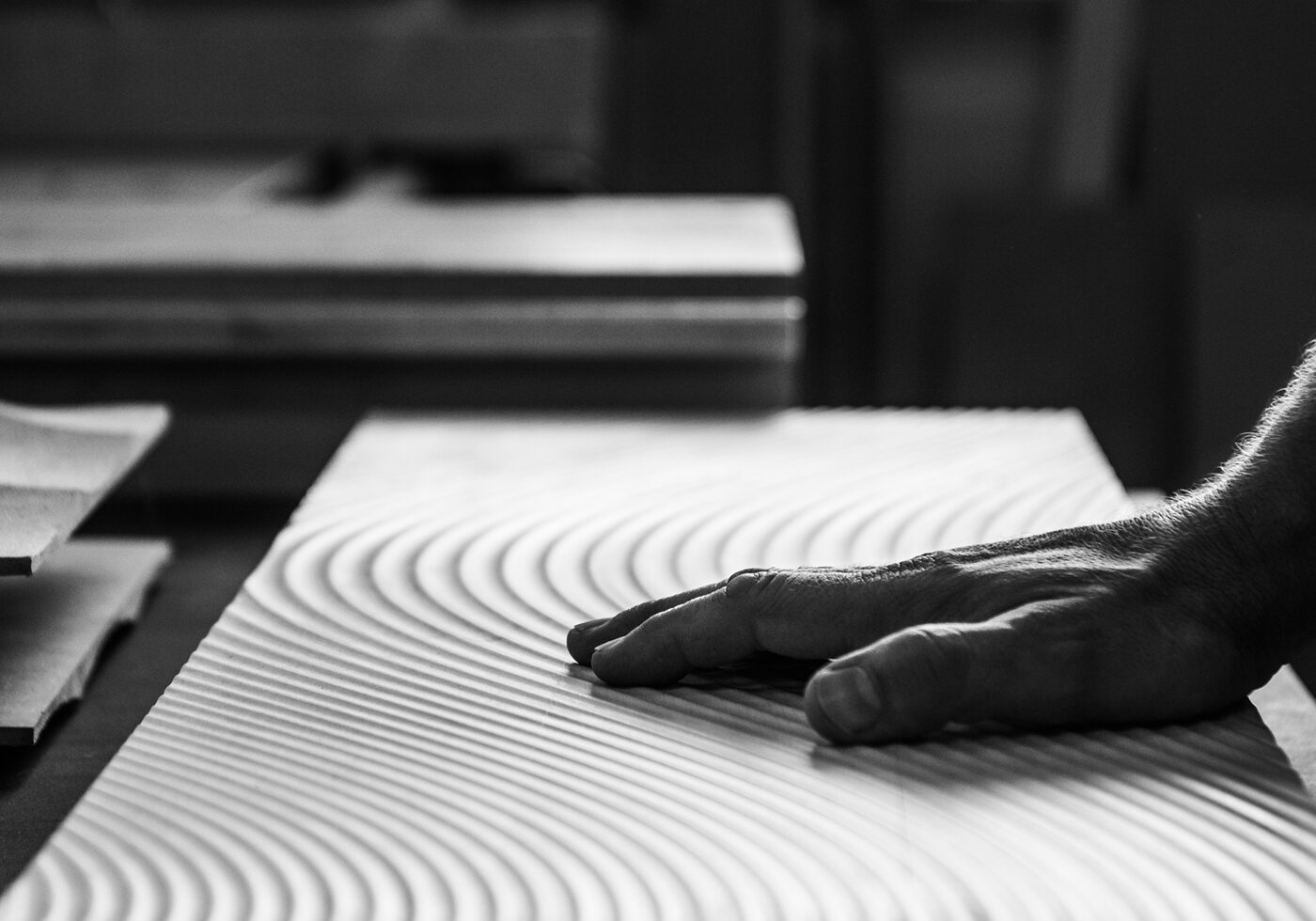 Delicate, engraved lines on wood with a hand gently touching the surface, captured in black and white.