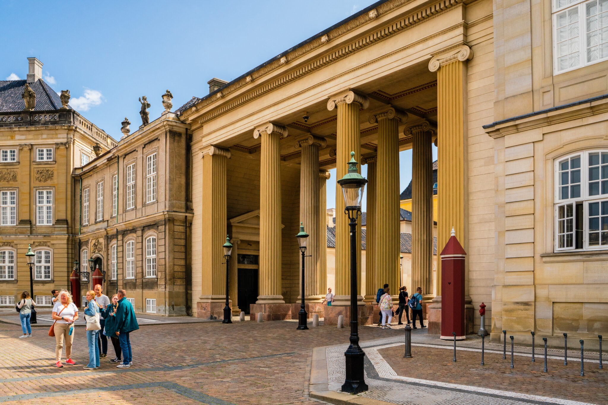 Cobbled street scene with people strolling past grand columns and historic buildings in Copenhagen.