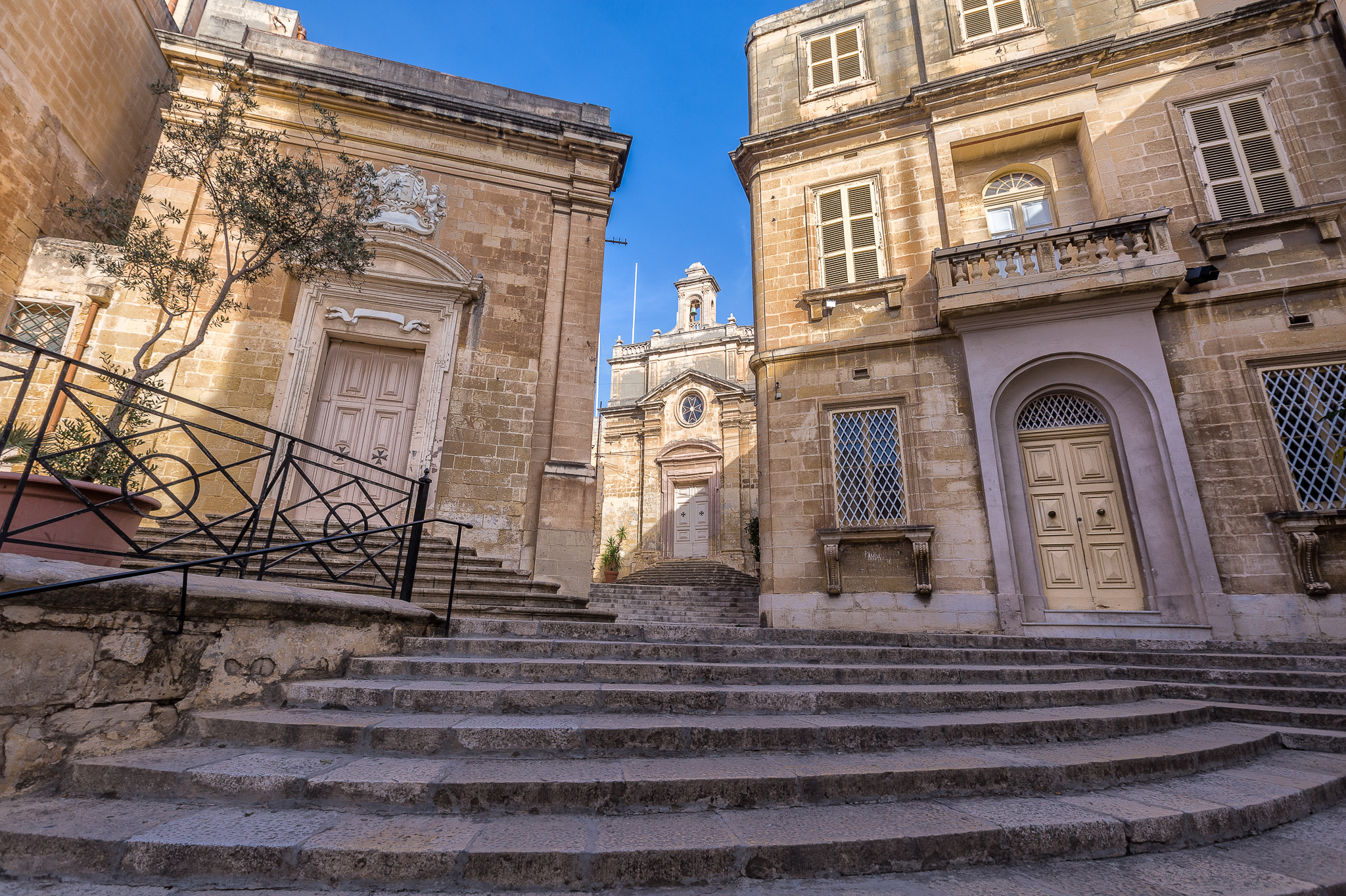 Stairs leading up to historic buildings in Birgu, featuring stone architecture and a clear blue sky.