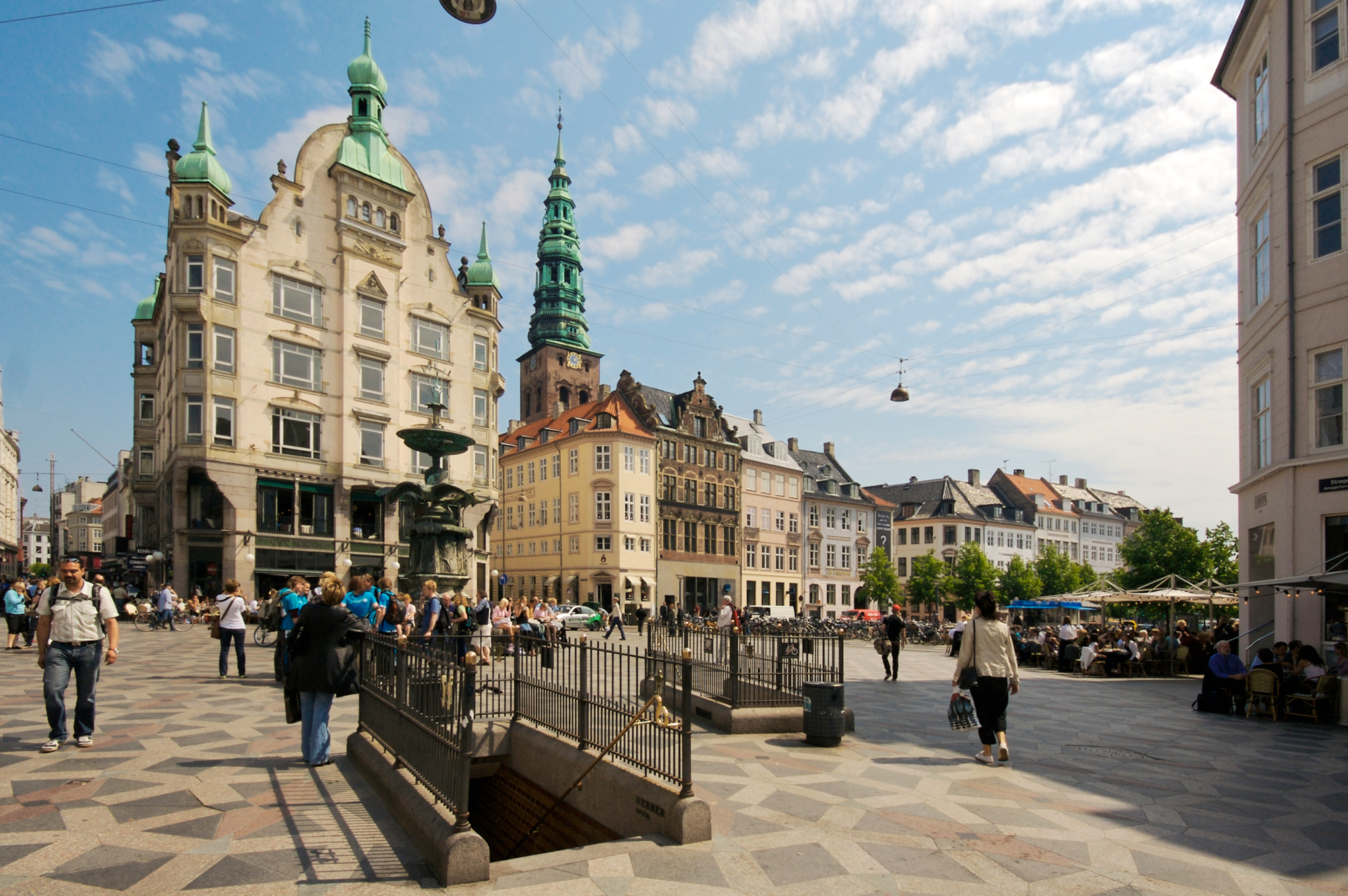 Bustling street scene in Copenhagen's Strøget, featuring historic buildings, a fountain, and people enjoying outdoor cafes.