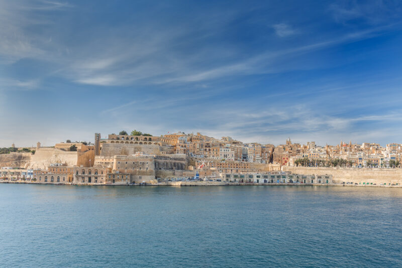 View of Birgu from the Grand Harbour, showcasing historic architecture along the waterfront under a blue sky.