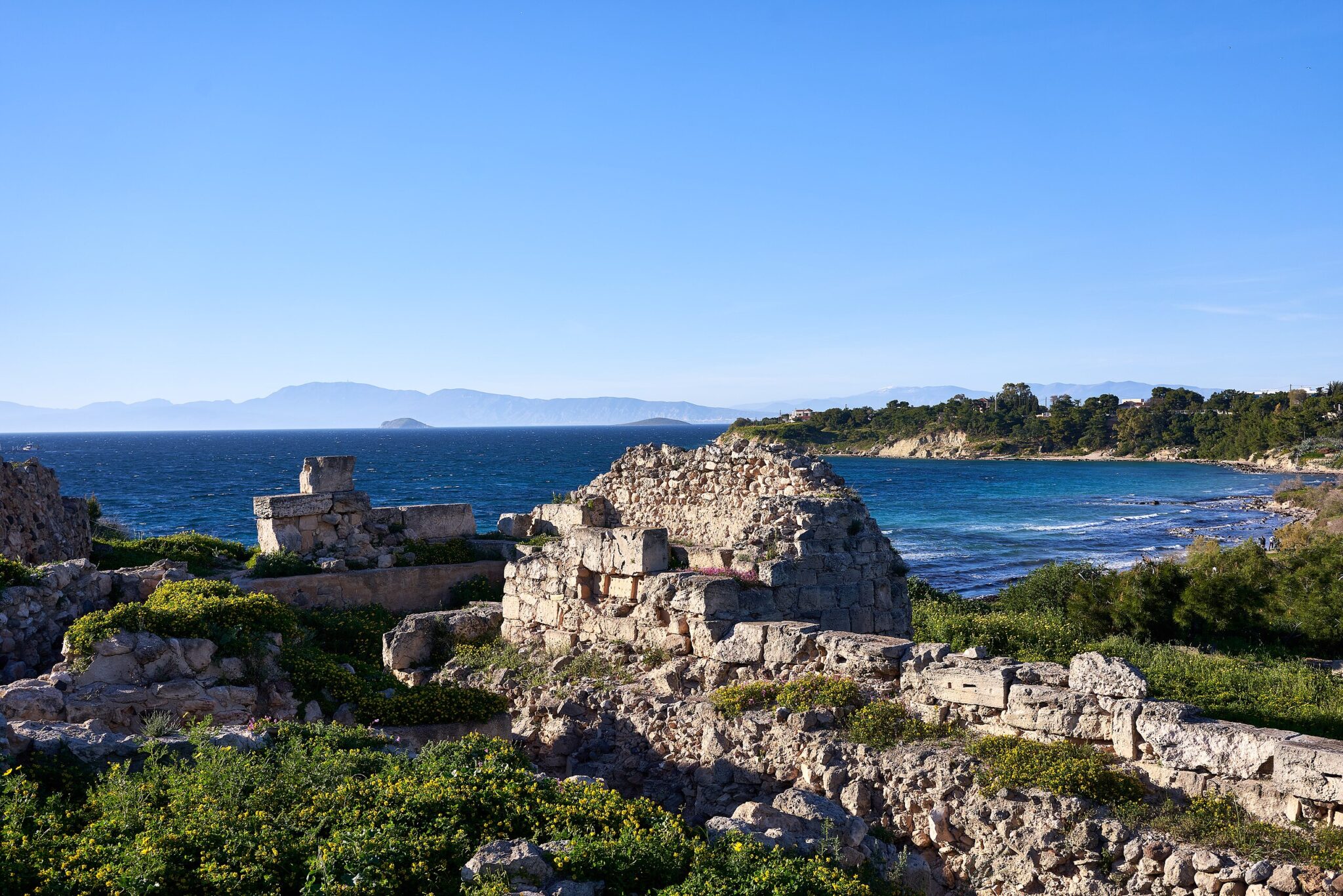 Ruins of the ancient acropolis of Aegina, with a coastal view and blue sky in the background.