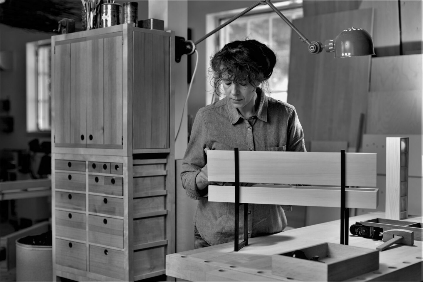 Tuulia Penttilä working in her studio, focused on a wooden project with tools and cabinetry in the background.