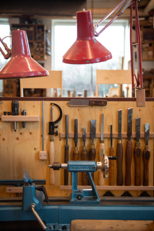 Woodworking tools neatly arranged on a wall in Fenhann's workshop, with red lamps illuminating the workspace.