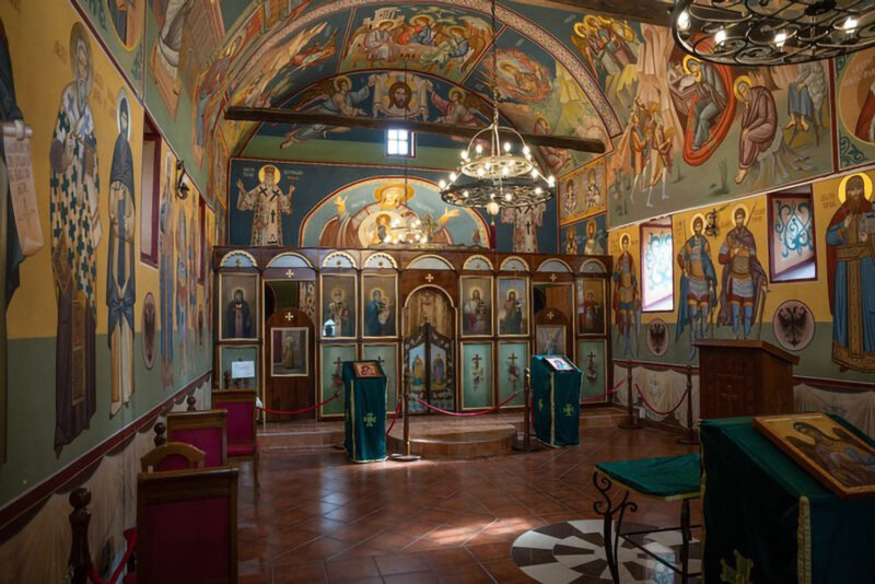 Interior of a church featuring colorful frescoes, wooden icons, and ornate chandeliers, creating a serene atmosphere.