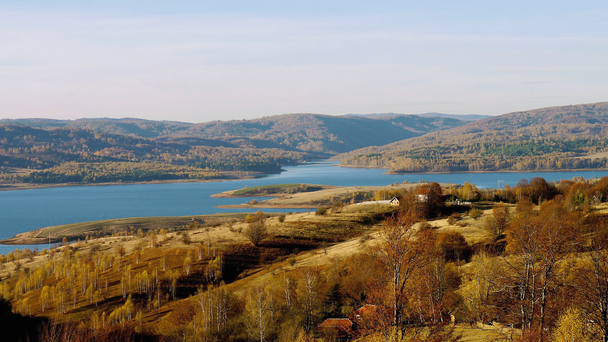 Scenic view of Lake Vlasina in Serbia, surrounded by rolling hills and autumn foliage under a clear blue sky.
