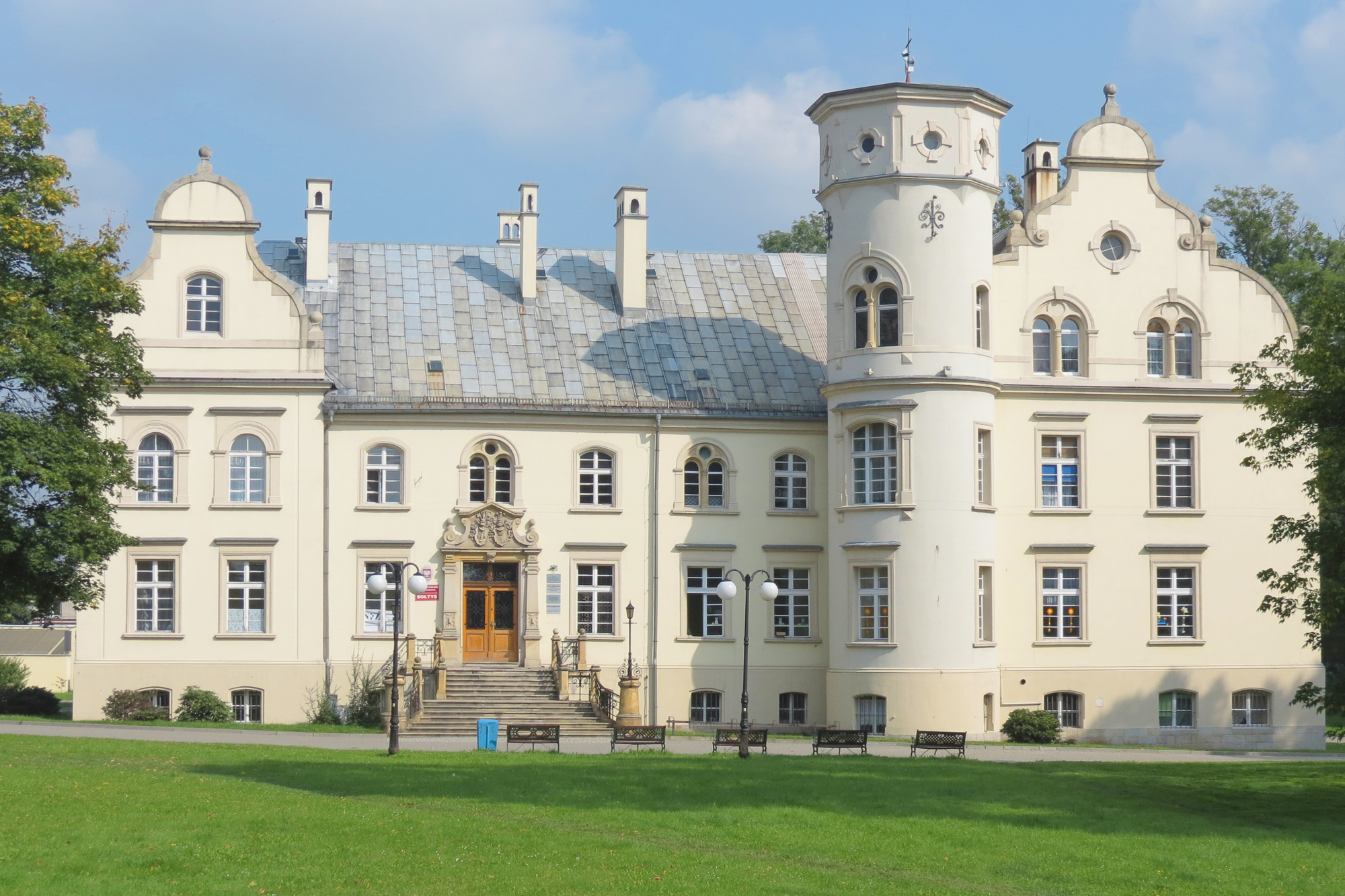Historic palace in Przyszowice with a light-colored facade, turret, and landscaped lawn in front.