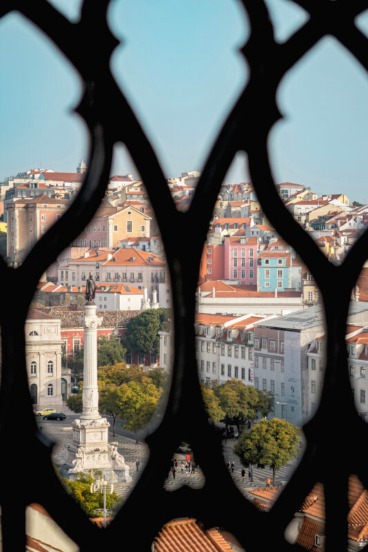 View of a colorful cityscape through a decorative lattice, featuring a monument and trees in the foreground.