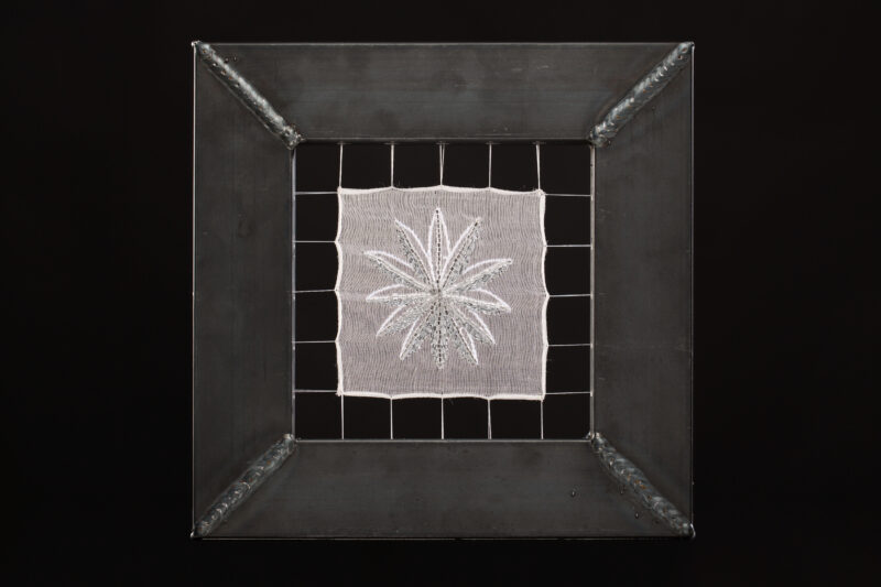 Embroidery of a star-like design framed in a metallic border, displayed against a black background.