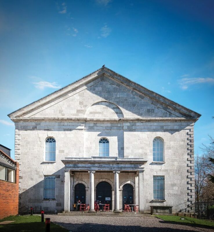 Neoclassical Georgian church facade of Triskel Arts Centre in Cork, featuring three arched entrances and outdoor seating.