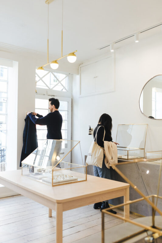 Bright, minimalist interior of ætla jewellery boutique in Edinburgh, featuring display cases and two customers browsing.