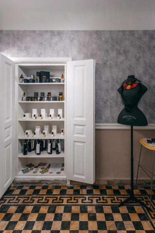 Open white cabinet displaying various bottles and products, with a black mannequin wearing a colorful necklace beside it.