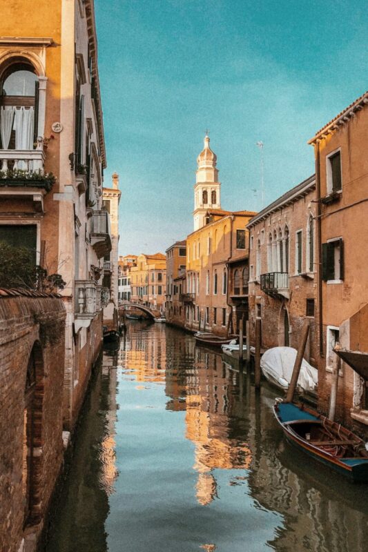 Canal in Venice reflecting colorful buildings and a bell tower under a clear blue sky, showcasing the city's artistic charm.