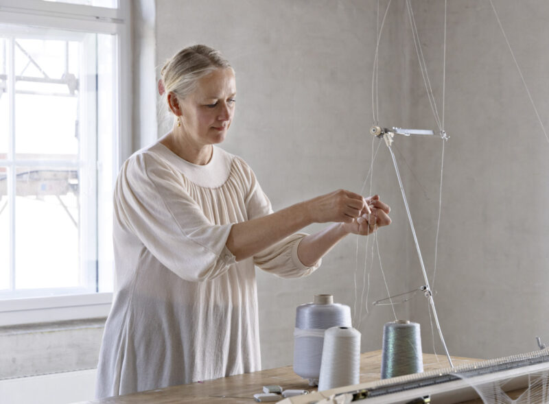 Iben Høj working on a design project, threading a needle with spools of thread on a table.