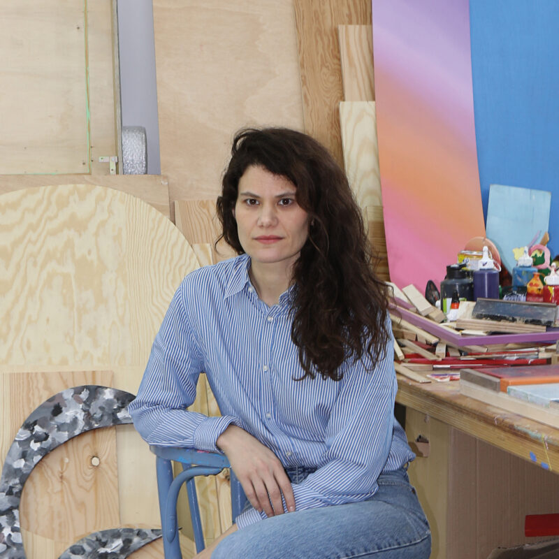 Artist Katharina Trudzinski seated in her studio, surrounded by wooden panels and art materials.