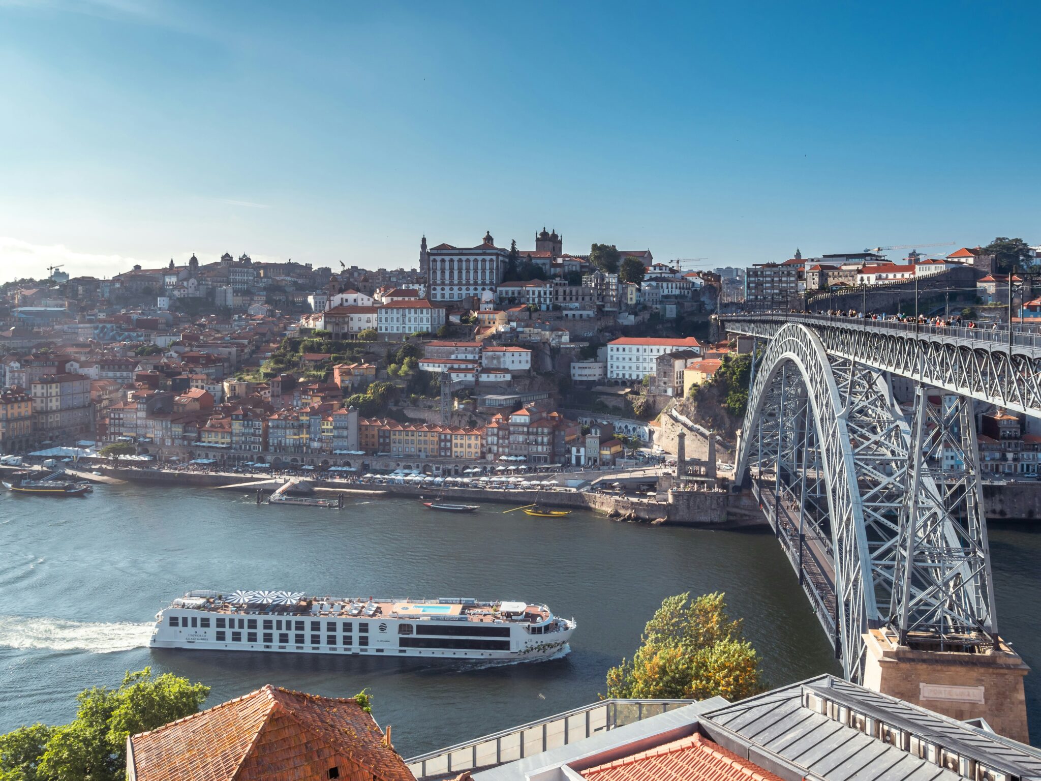 View of Porto, Portugal, featuring the Dom Luís I Bridge and a riverboat on the Douro River under a clear blue sky.