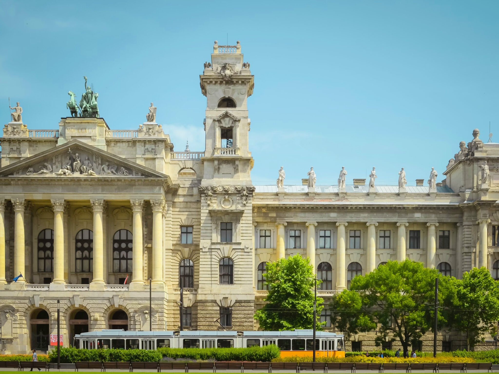 Historic building with ornate architecture, featuring a tram in front and clear blue sky above.