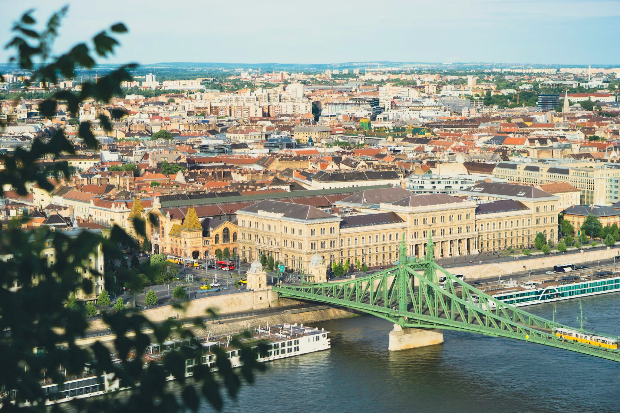 Panoramic view of a cityscape featuring a green bridge over a river, with buildings and rooftops in the background.