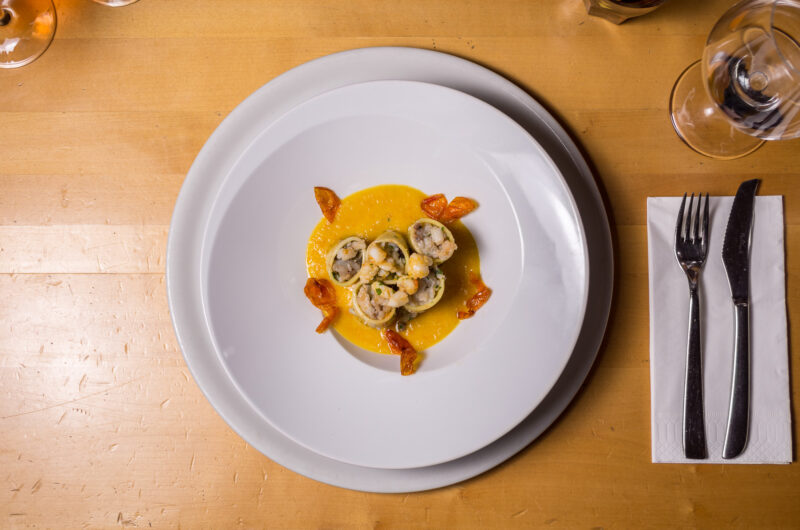 Plate of shrimp and pasta on a yellow sauce, garnished with dried tomatoes, on a wooden table in Vienna.