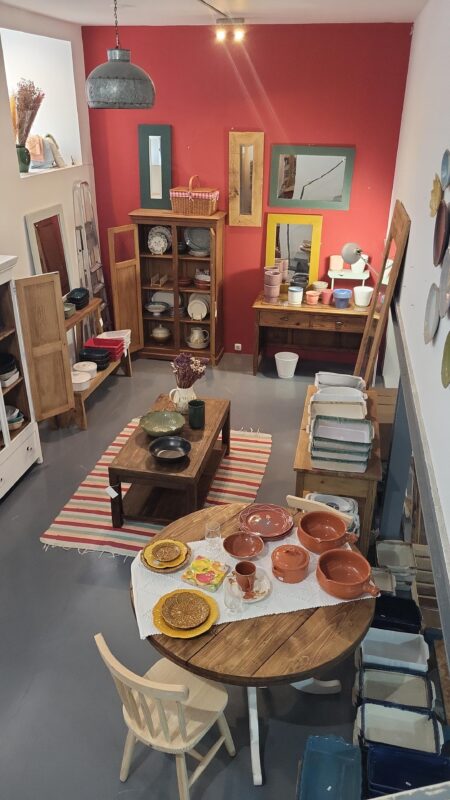 Artisan pottery and wooden furniture displayed in a cozy shop with red walls and various decorative items.