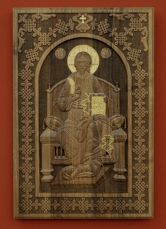 Wooden relief of Christ seated on a throne, holding a book, framed by intricate carvings against a red background.