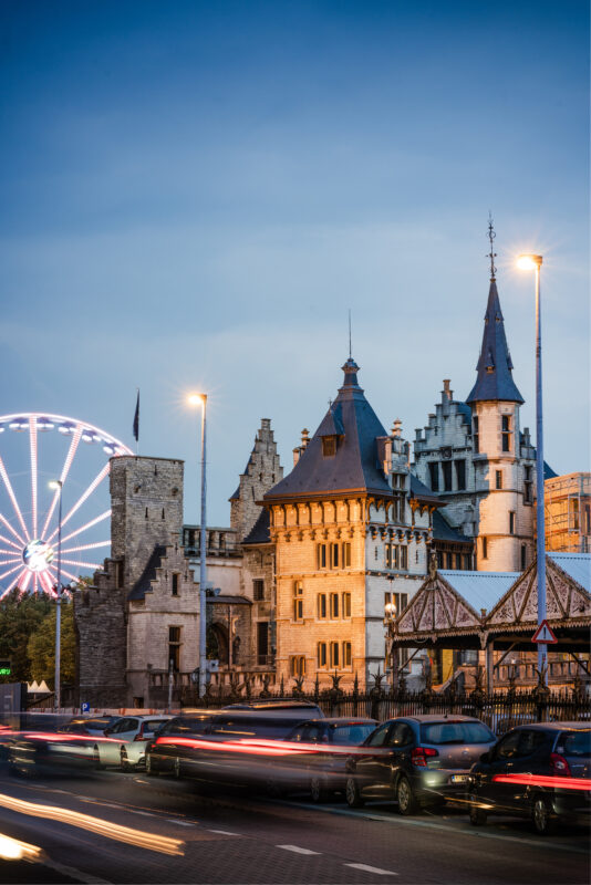 Het Steen castle partially obscured by buildings, with a ferris wheel in the background and evening lighting.