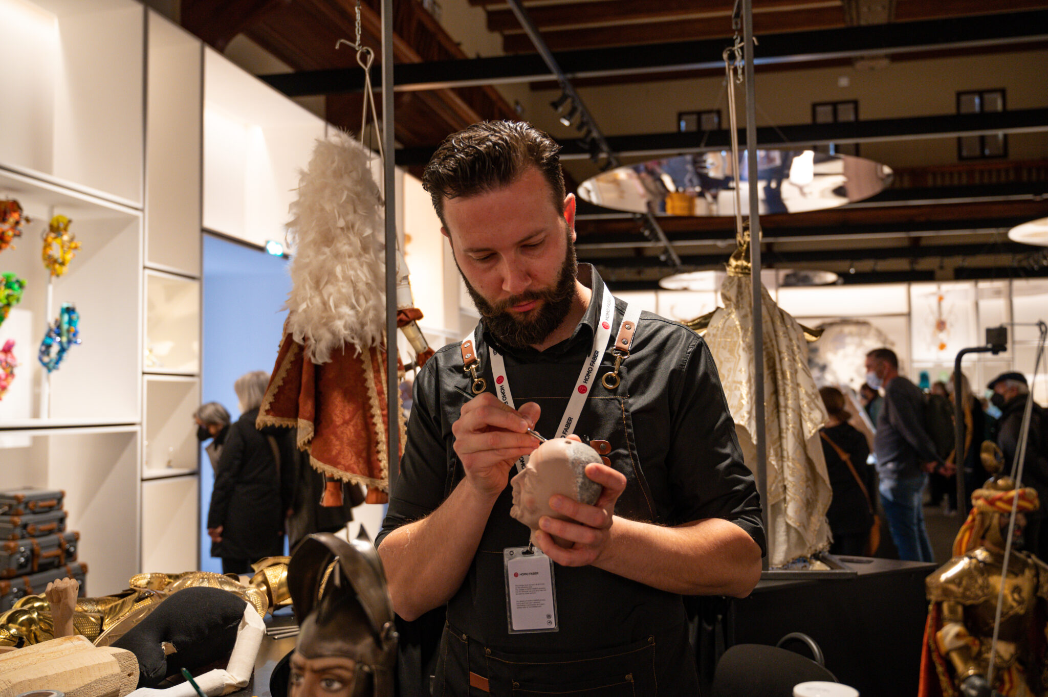 Daniel Mauceri working on a sculpture at the Homo Faber Exhibition in Venice, surrounded by artistic displays.