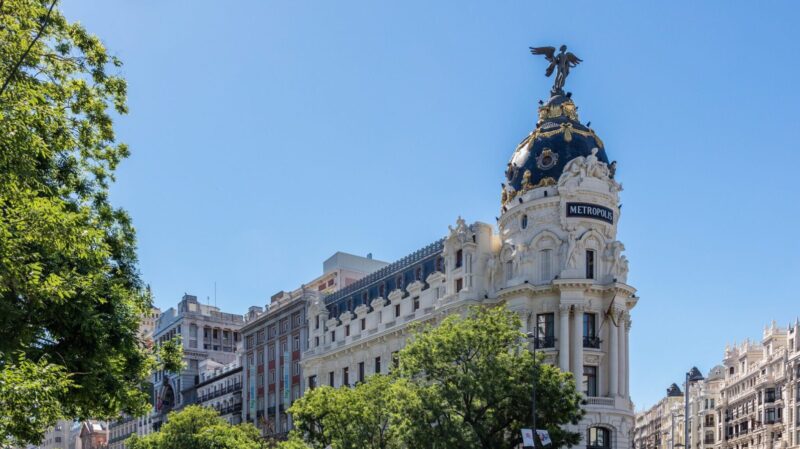 Edificio Metrópolis on Calle de Alcalá in Madrid, featuring its iconic dome and surrounding trees, under a clear blue sky.