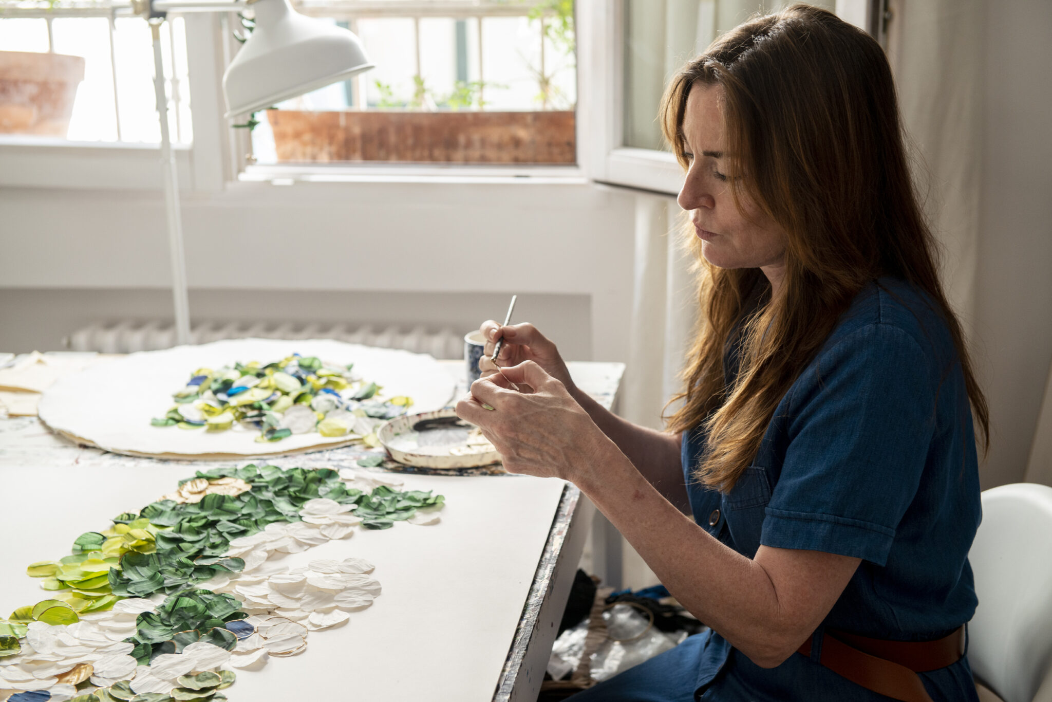 Artist Ana Paúl creates floral art, carefully arranging colorful petals on a large canvas in a bright studio.