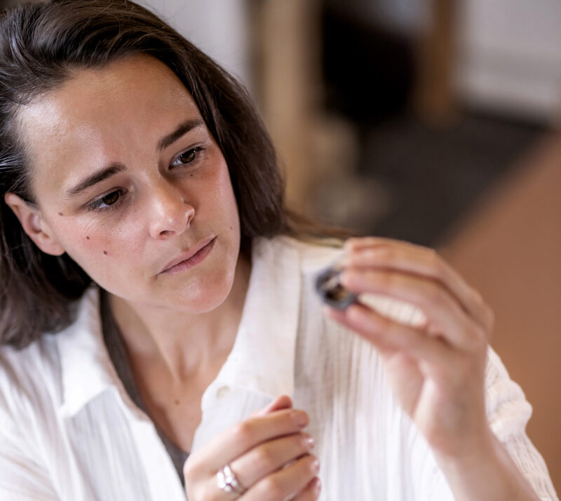Woman examining a small object closely, wearing a white shirt, in a softly lit indoor setting.