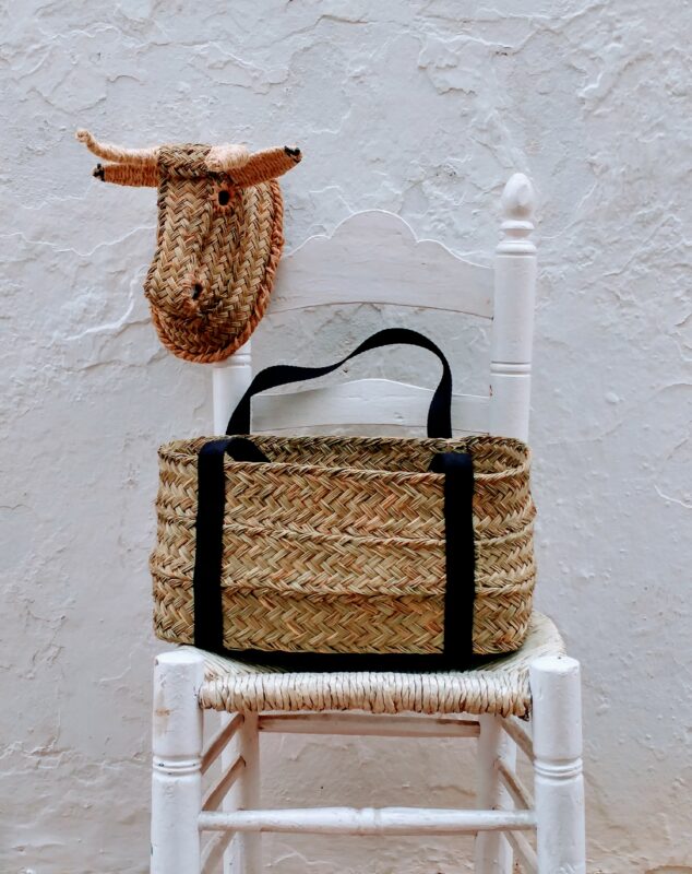 Woven bull's head and a straw basket on a white wooden chair, symbolizing Andalusian culture.