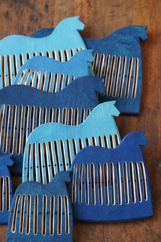 Wooden combs shaped like birds in various shades of blue arranged on a wooden surface.