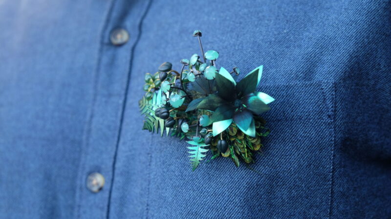 Brooch designed by Marie Grimaud featuring green foliage and flowers, worn on a blue shirt.