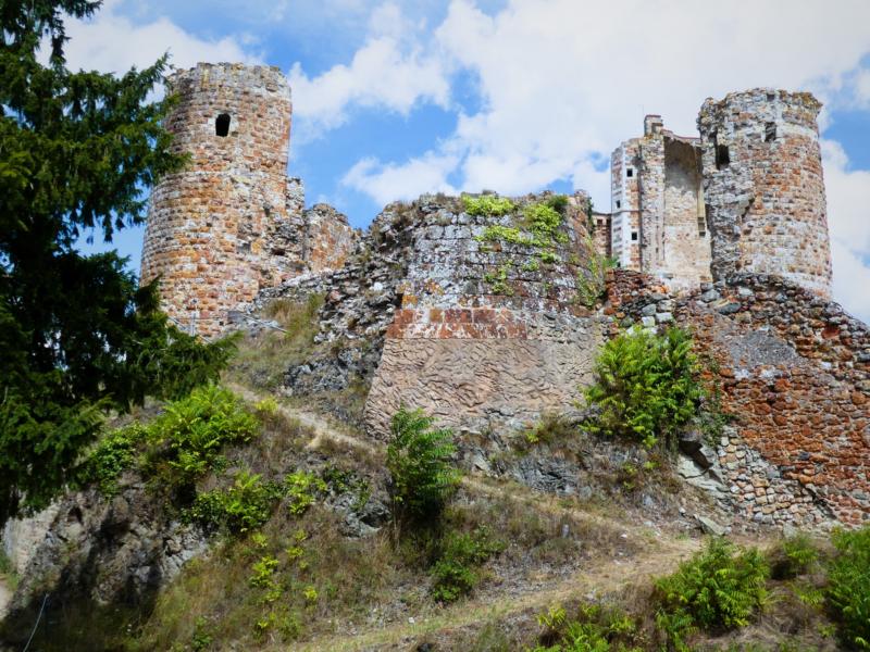 Ruins of a stone castle on a hillside, surrounded by greenery and under a partly cloudy sky.