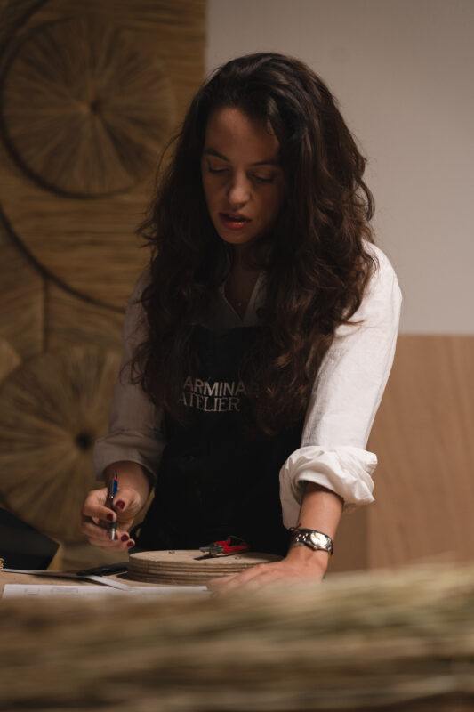 Gabriela Sagarminaga working on a wooden project, wearing an apron, with tools and materials on a table.