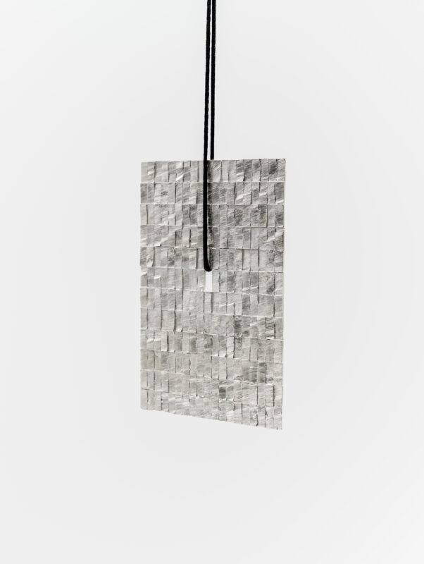 Textured silver paper hanging at an angle, featuring a grid pattern, part of Annie Sibert's 2024 lighting score.
