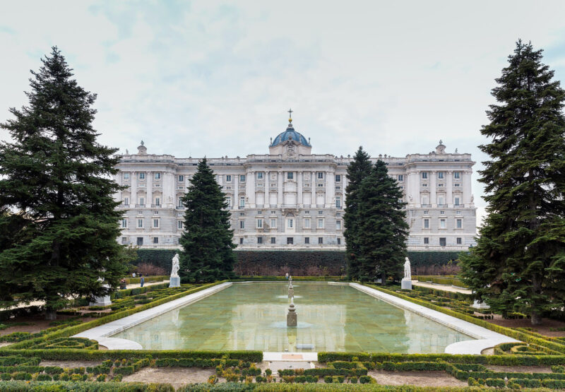 Palacio Real in Madrid, surrounded by manicured gardens and tall trees, reflecting in a pond, taken on December 27, 2014.