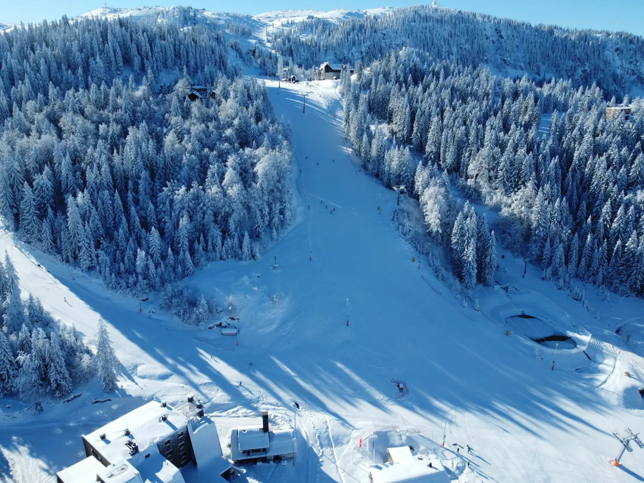 Snow-covered mountains of Sarajevo with ski slopes and pine trees, showcasing a winter landscape.