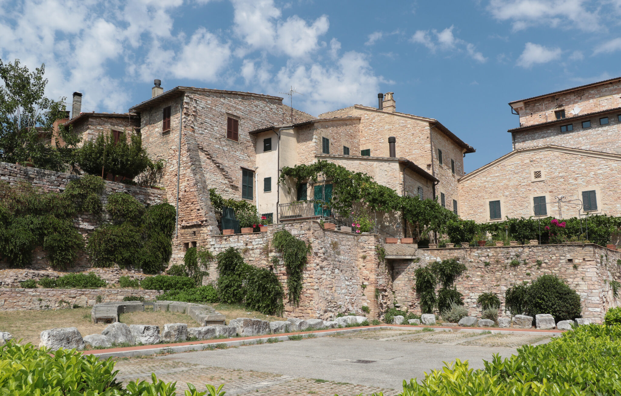 Historic stone buildings with greenery in Spello, Italy, under a partly cloudy sky.