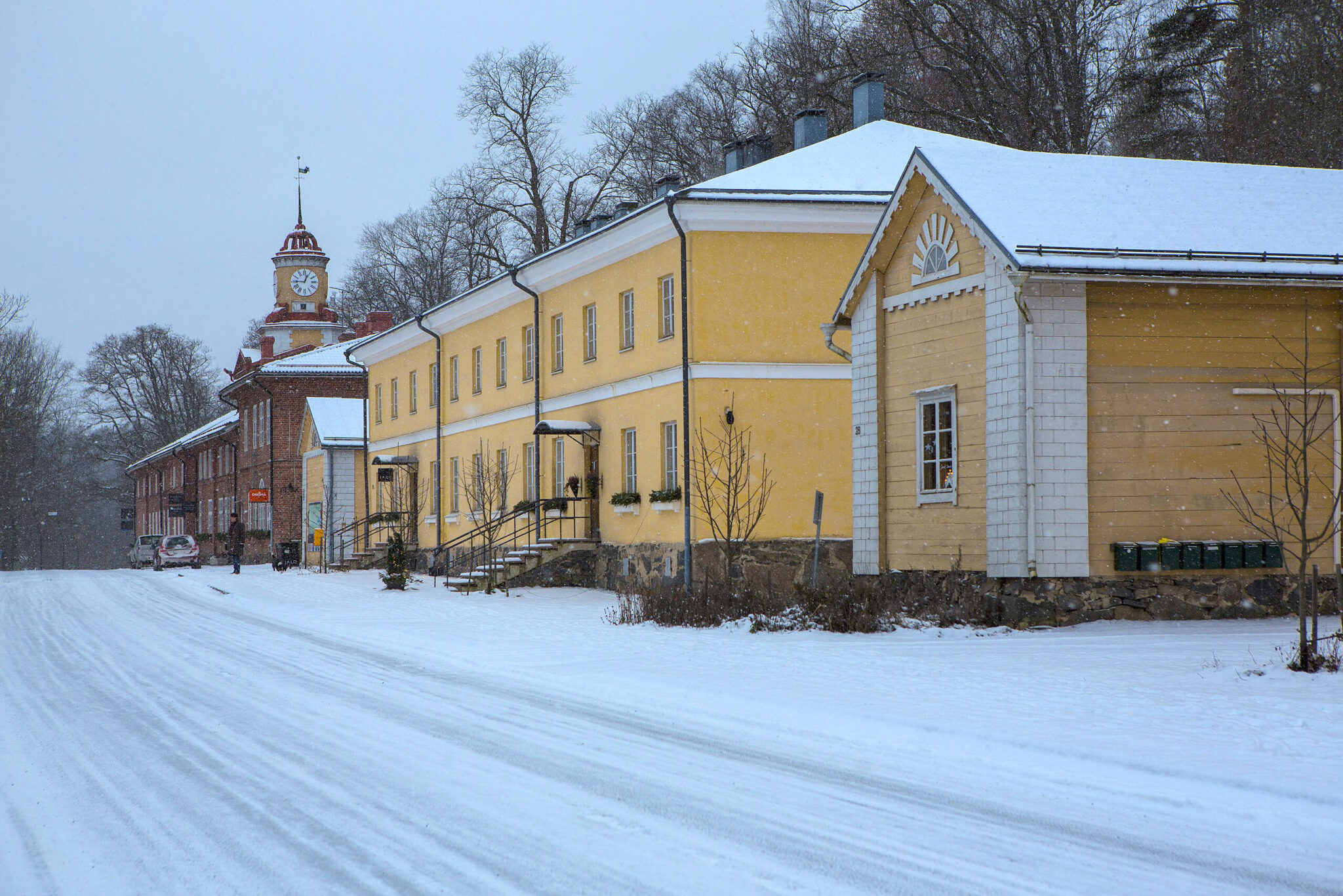 Snow-covered street in Fiskars village, featuring yellow and white buildings, with a clock tower in the background.