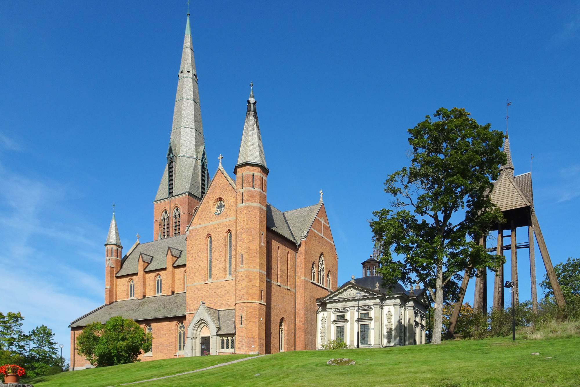 Floda Church in Södermanland, Sweden, featuring red brick architecture and a tall spire against a clear blue sky.