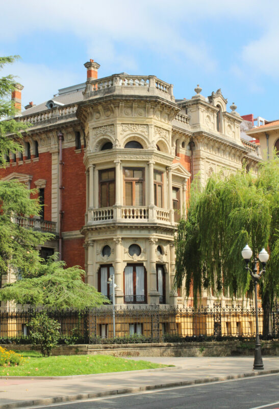 Historic building with ornate architecture, featuring intricate details and large windows, surrounded by greenery.