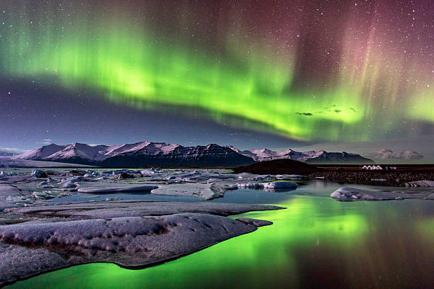 Intense polar lights illuminate a glacier lagoon in Iceland, reflecting on the water's surface.