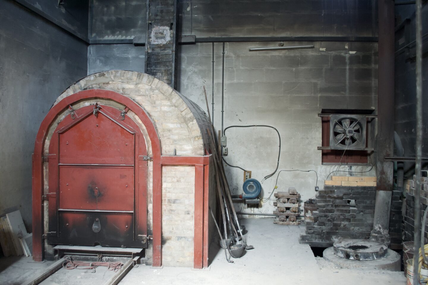 Kiln rebuilt after 20 years, featuring a red door and surrounding tools in a workshop setting.