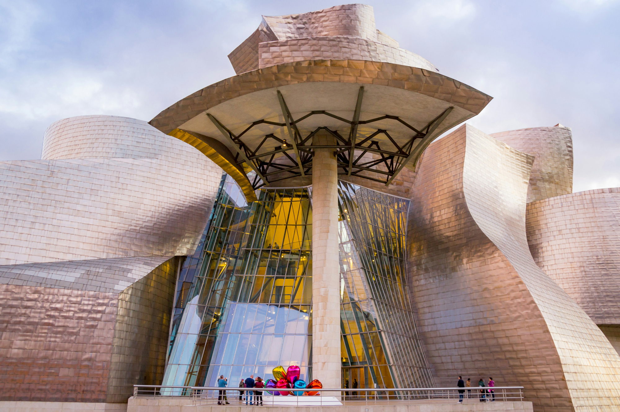 Guggenheim Museum's unique architecture with metallic curves and large glass entrance, featuring colorful sculptures in fr...