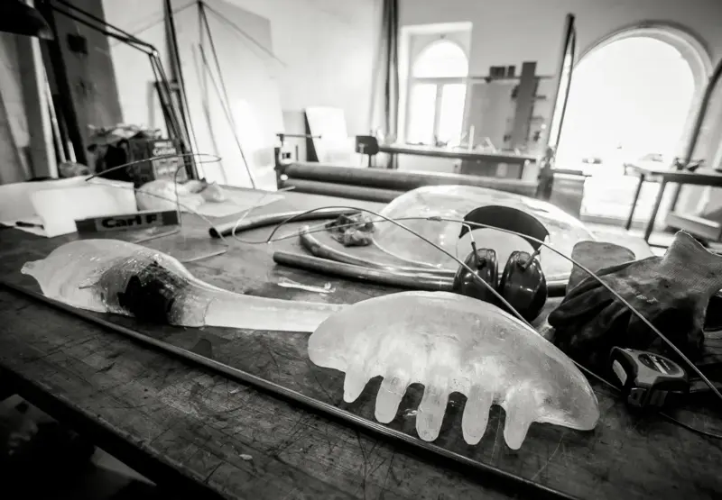 Artistic glass sculptures resembling jellyfish on a workshop table, with tools and materials in a bright studio.