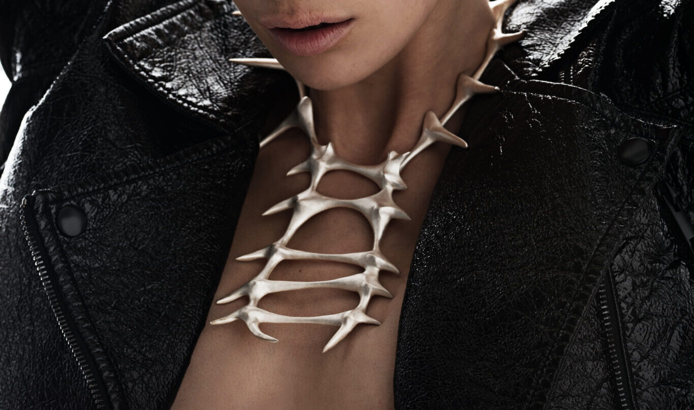 Metal bone necklace resting on bare skin, worn with a black leather jacket, showcasing Hintsanen's unique design.