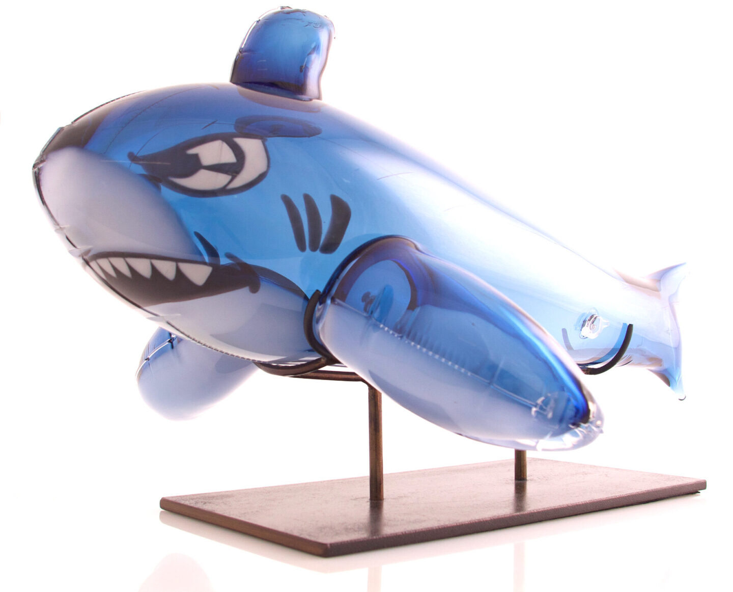 Glass sculpture of a blue inflatable shark with a fierce expression, mounted on a wooden base.