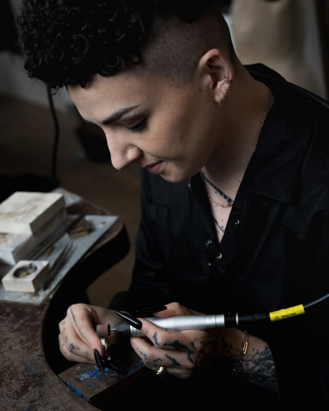 Cameron focused on a crafting tool, working at a desk with tools and materials around.