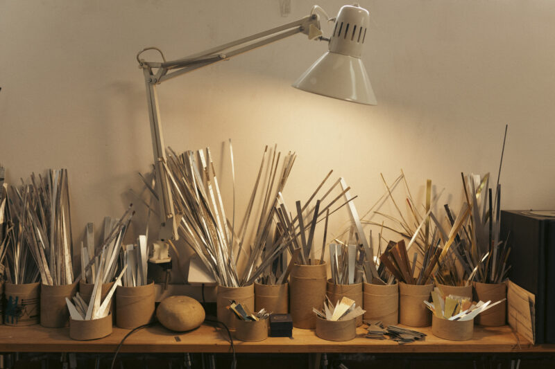 Raw materials in various containers and scattered on a workbench, illuminated by a lamp.